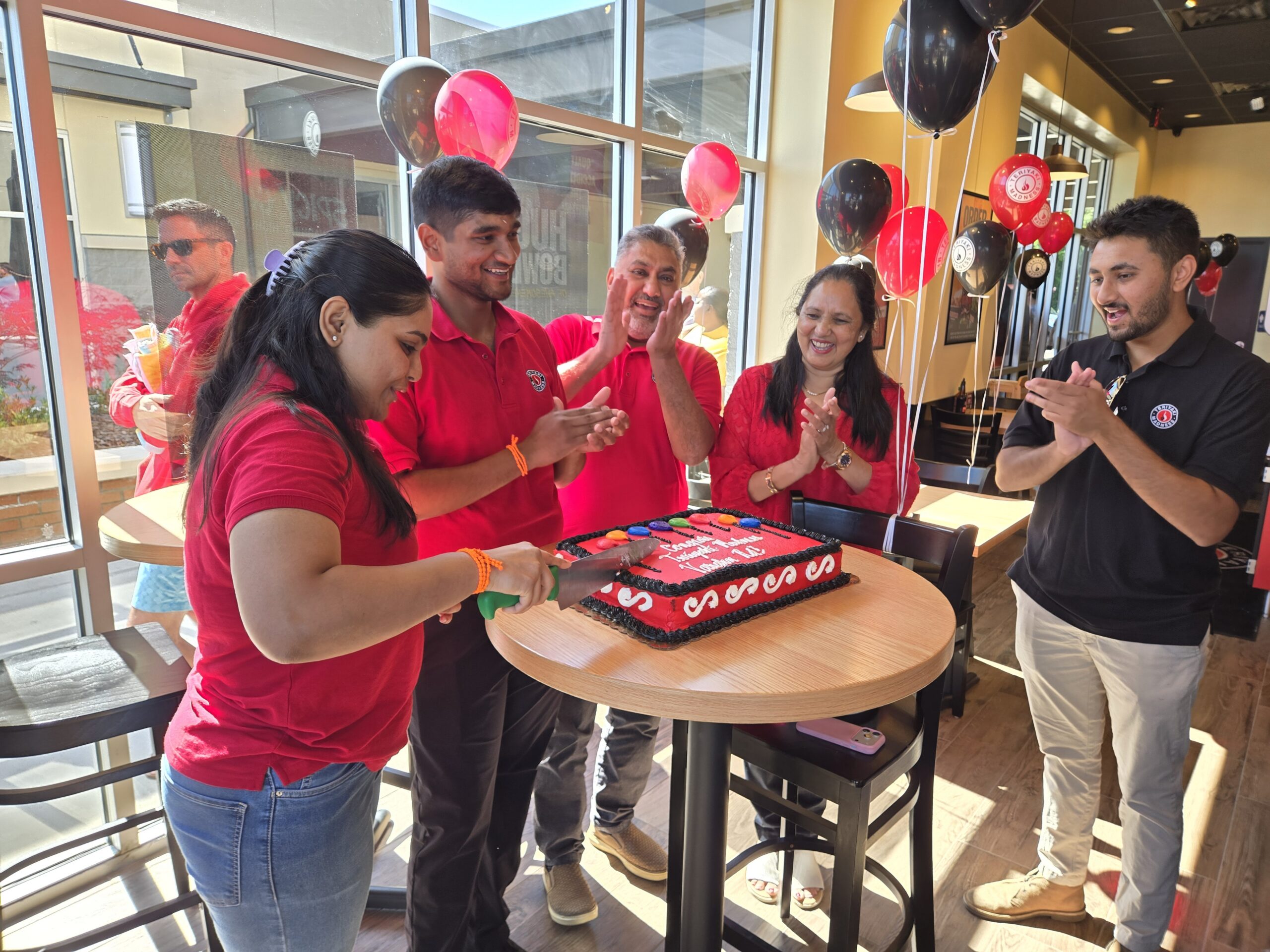 A group around a cake celebrating the opening of Teriyaki Madness